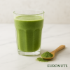Ένα ποτήρι smoothie/ρόφημα με alfalfa σε φωτεινή επιφάνεια, δίπλα λίγη σκόνη ή κουταλάκι, EURONUTS κάτω δεξιά